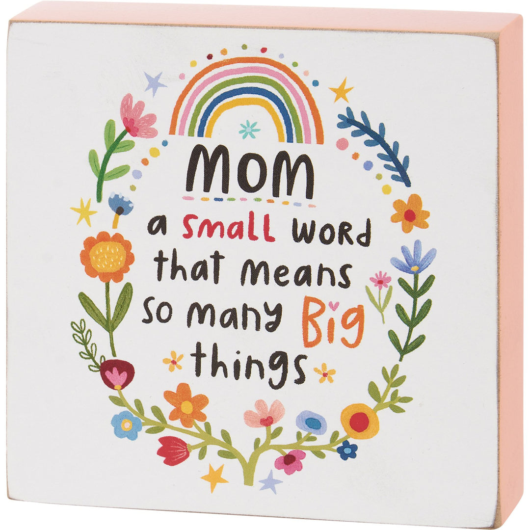 Wood block sign with pink sides displaying the text Mom A Small Word Big Things.