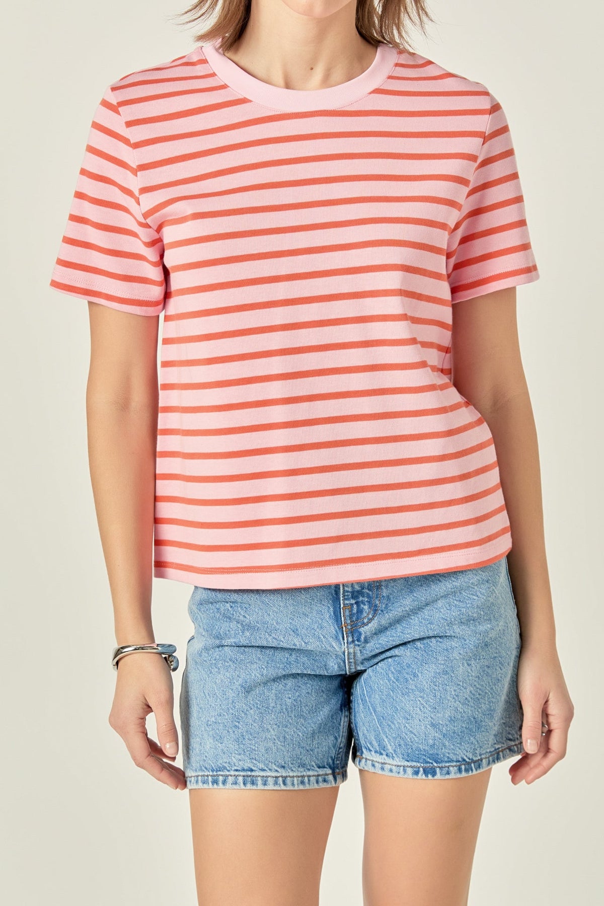 Woman wearing the Allison Stripe T-shirt in pink and orange with blue denim shorts.