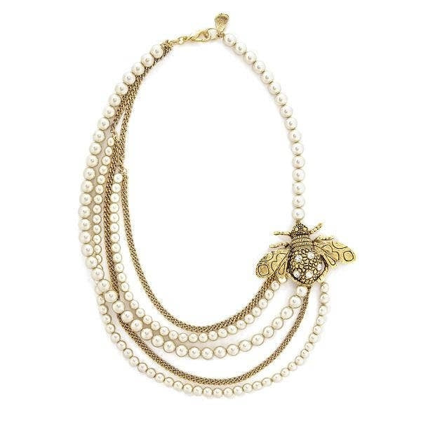 Kiata layered necklace with white pearls, gold-tone chains, and a detailed gold bee pendant.