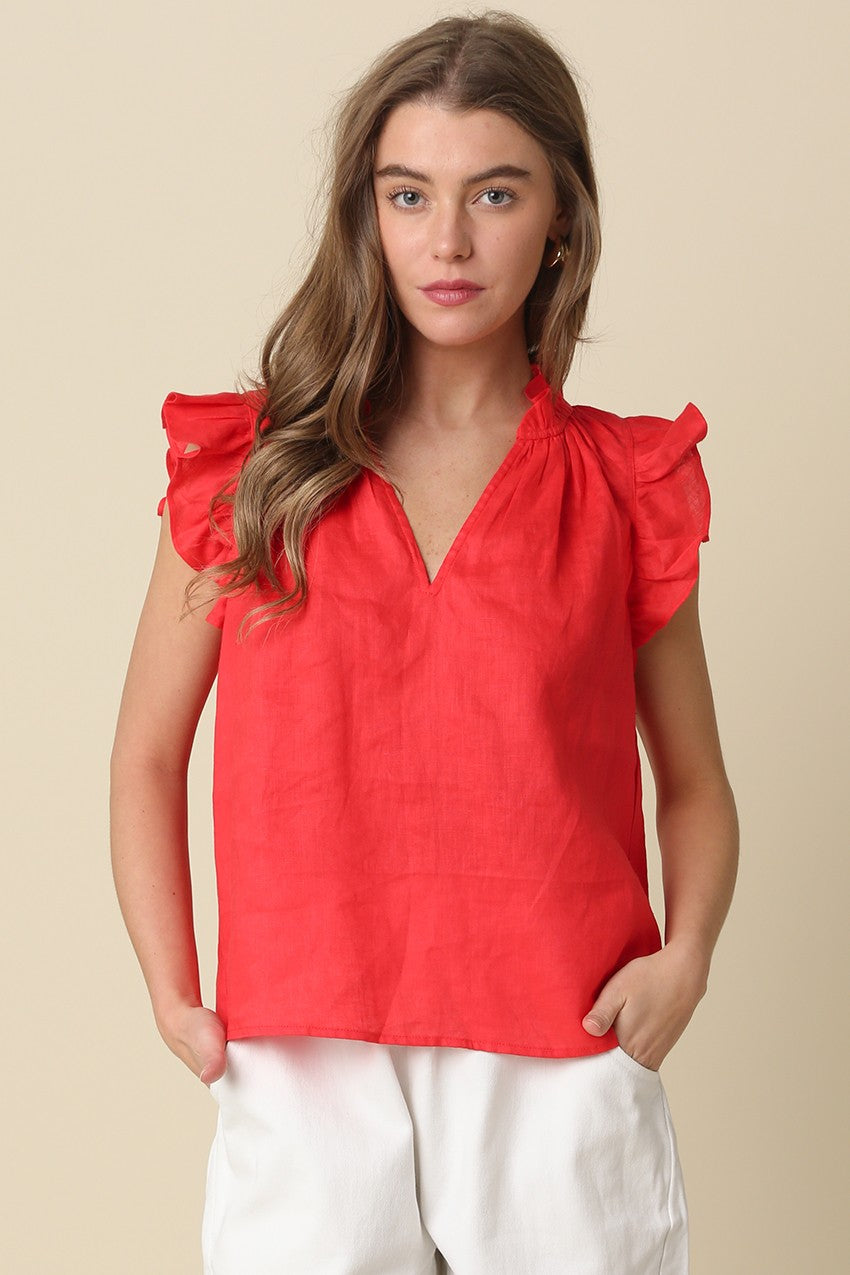 A woman wears a red linen Heidi blouse with ruffle sleeves and a V-neckline.
