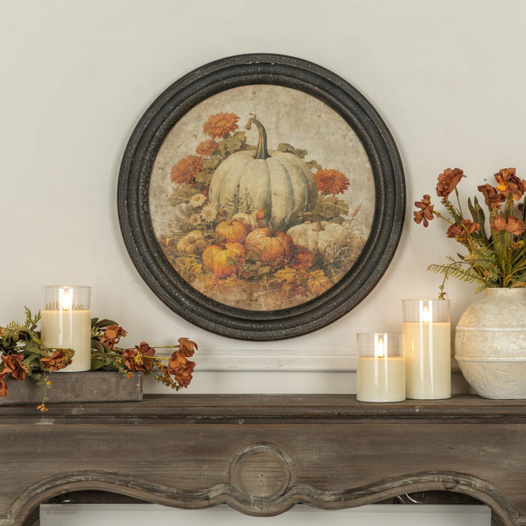Round framed pumpkin patch print on a wall above a mantel with candles and autumn flowers.