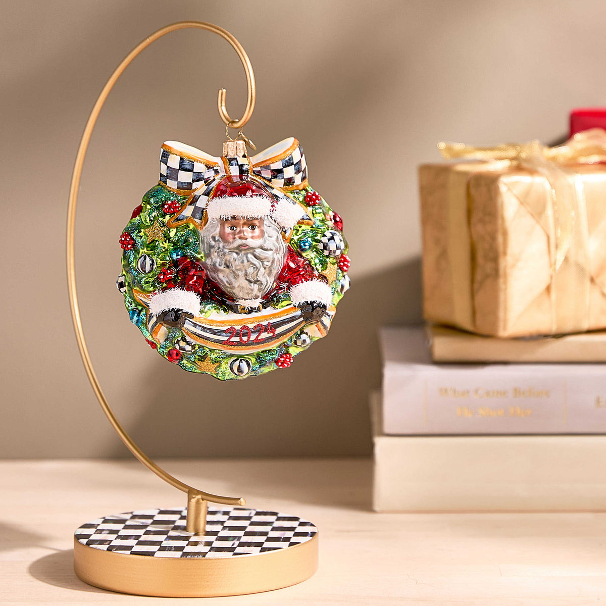 Gold metal ornament stand with a checkered base holding a Santa wreath ornament.