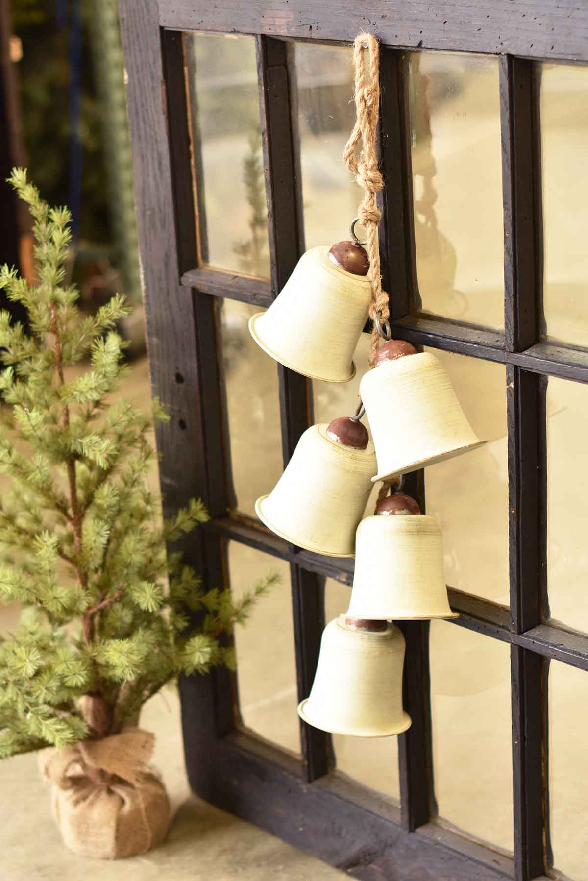 Cream-colored ceramic bells with brown tops hang from a jute rope on a dark wooden window frame.