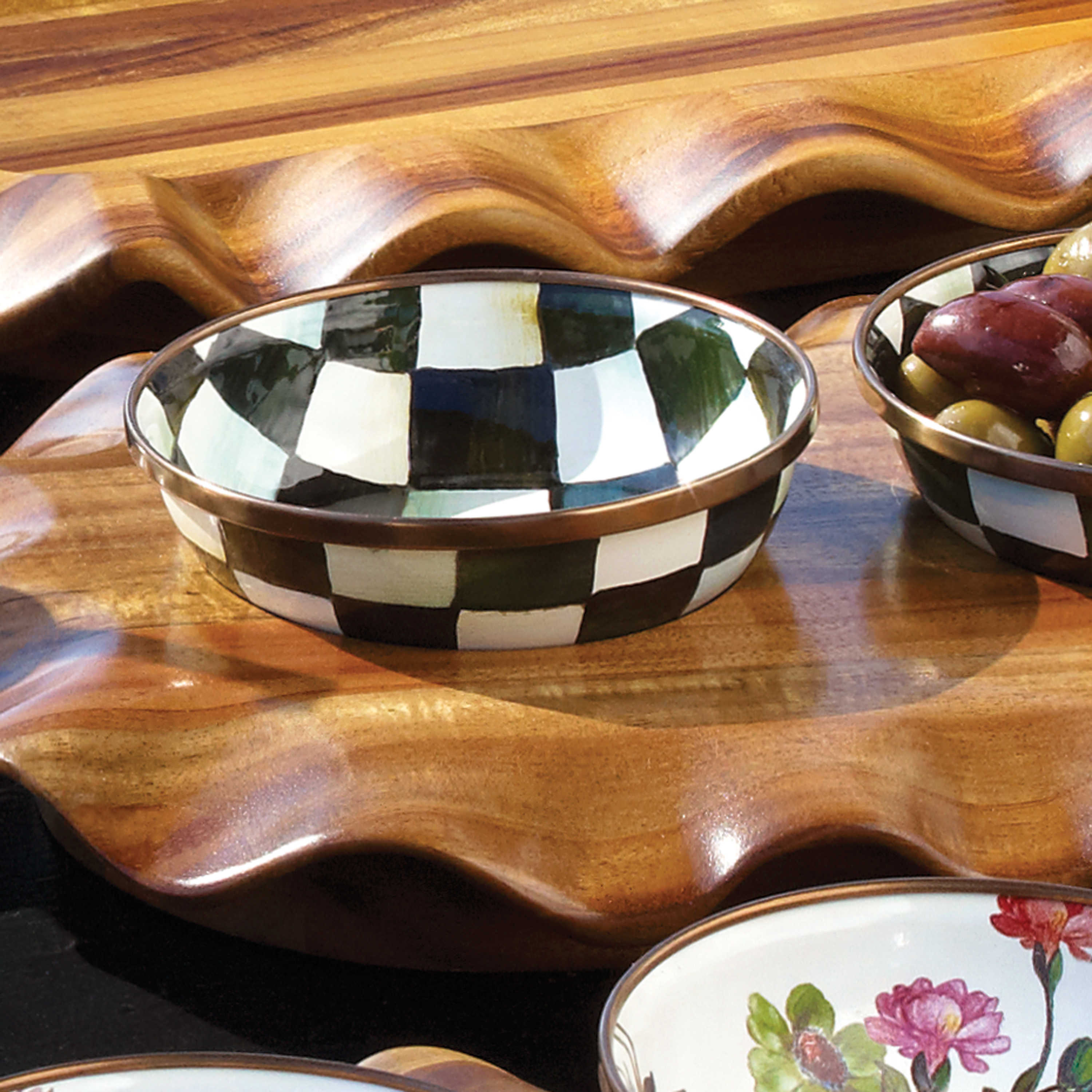 Hand-painted Courtly Check relish dish with a bronzed stainless steel rim on a wooden tray.