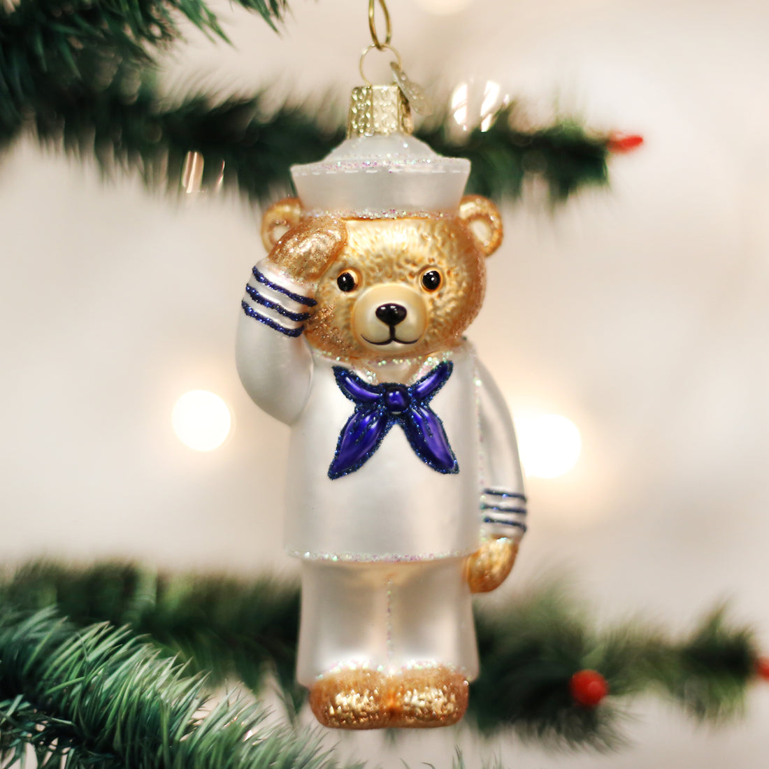 Glass Navy Bear Christmas ornament in a white sailor uniform saluting on a green tree branch.