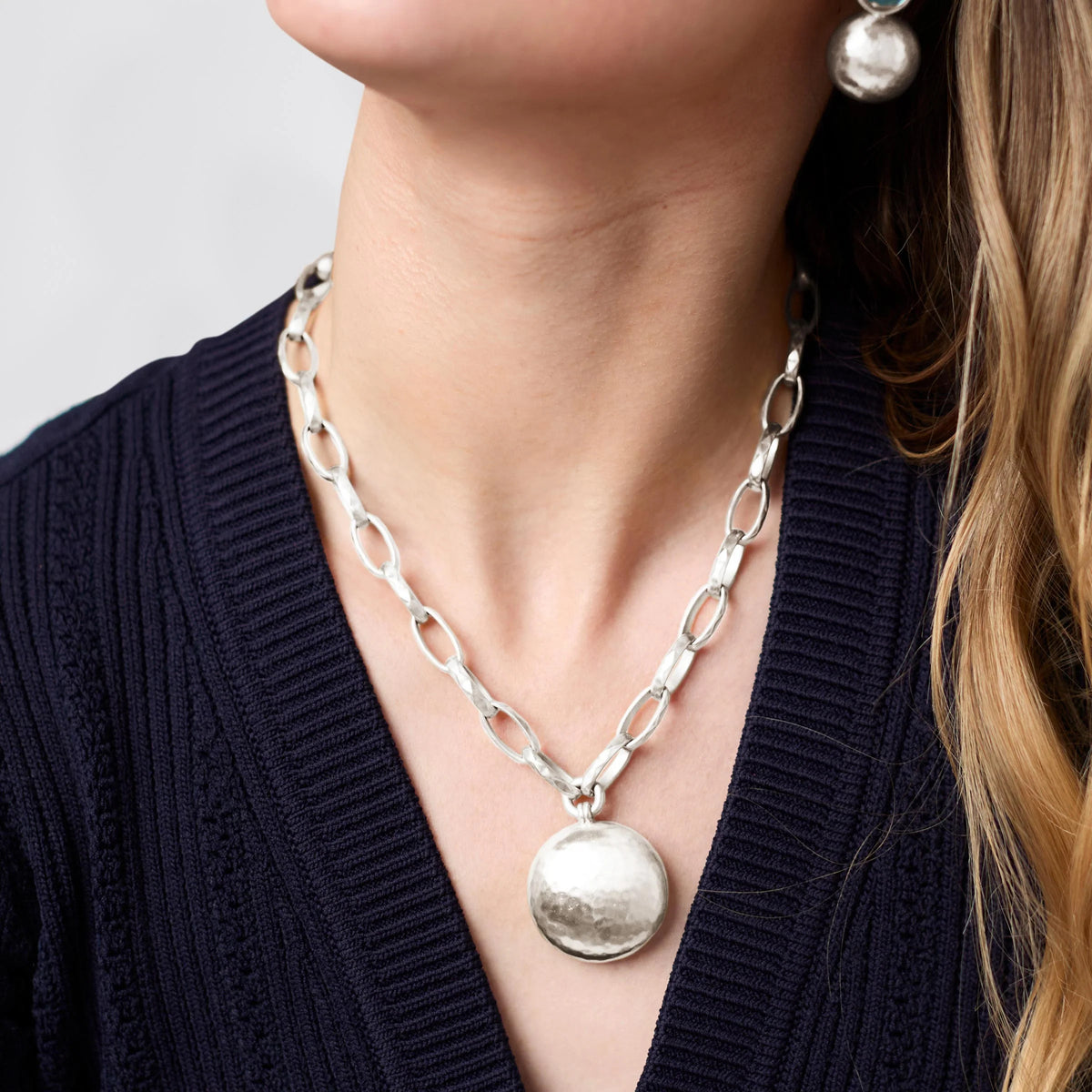 Woman wearing the Solara Necklace, a silver link chain with a large hammered round pendant.