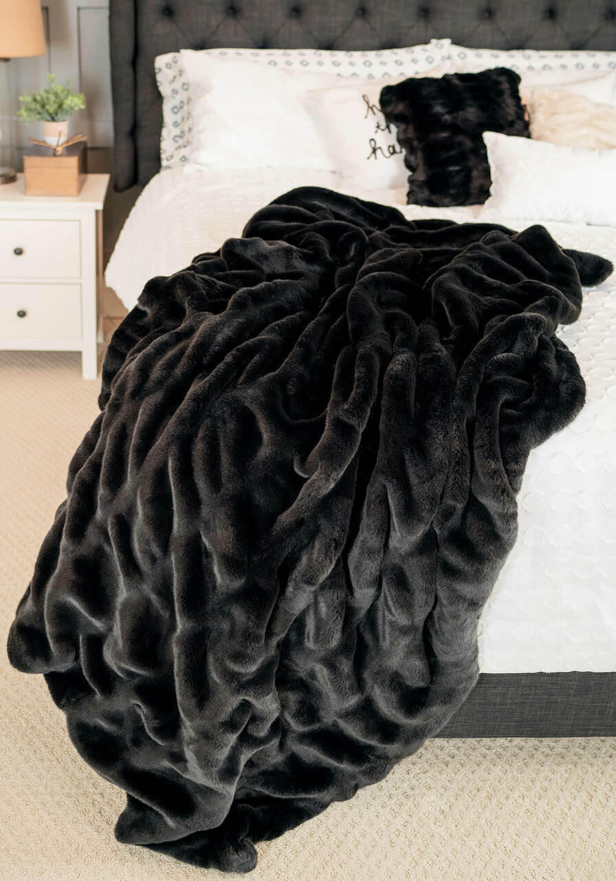 Couture Throw Onyx Mink faux fur blanket draped over a white bed with matching black pillows.