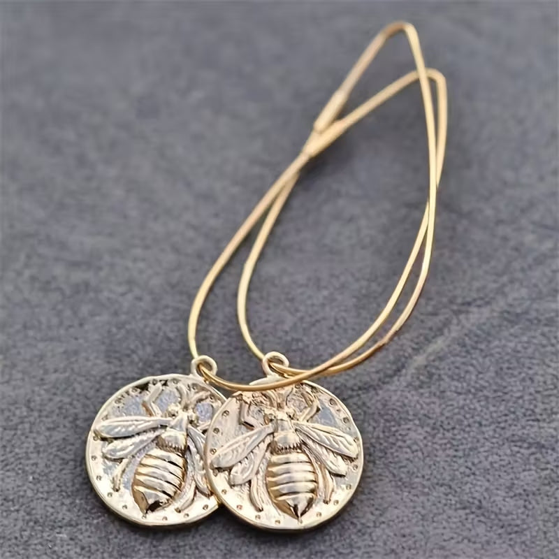Boho-Chic gold-tone round pendant earrings featuring a detailed bee pattern on long wire hoops.