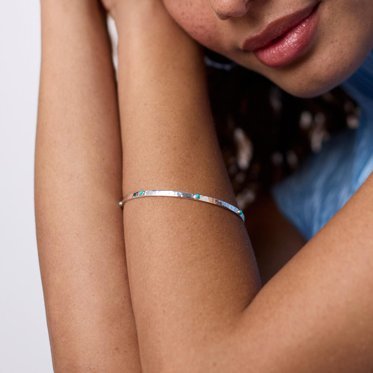 Close-up of a person wearing a thin, hammered silver Crescent Stone Bangle with turquoise accents.