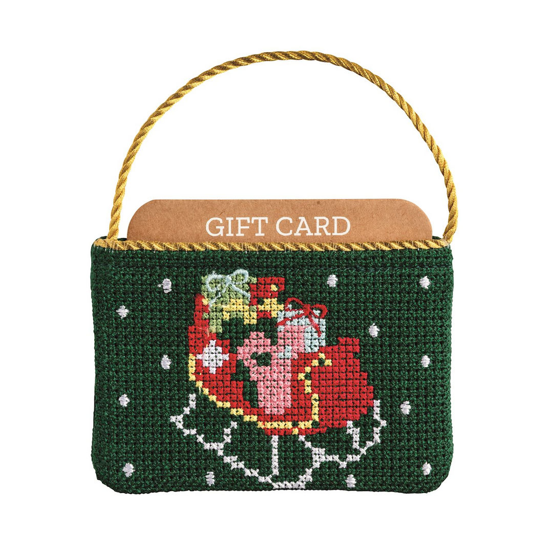 Green needlepoint gift card pouch with a red sleigh design and gold cord hanger.