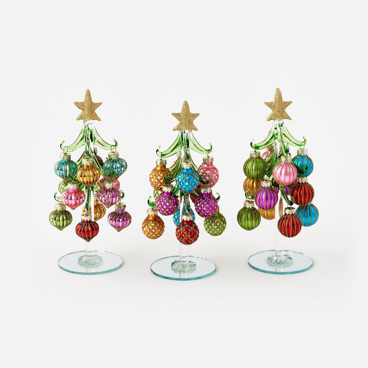Three handmade glass Christmas trees with colorful ornaments and gold star toppers.