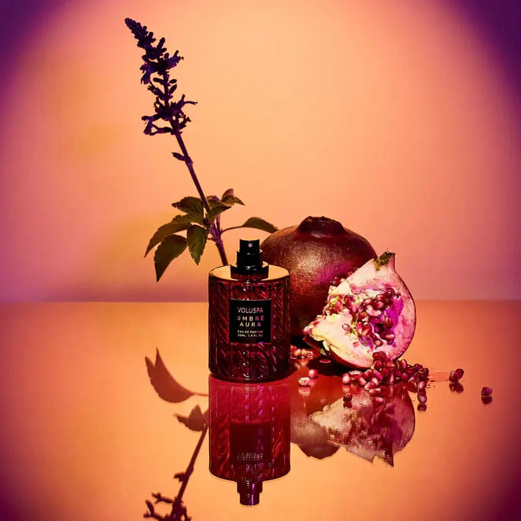 Glass bottle with amber liquid labeled Ombre Aura 55ml perfume featuring pomegranate and patchouli notes.