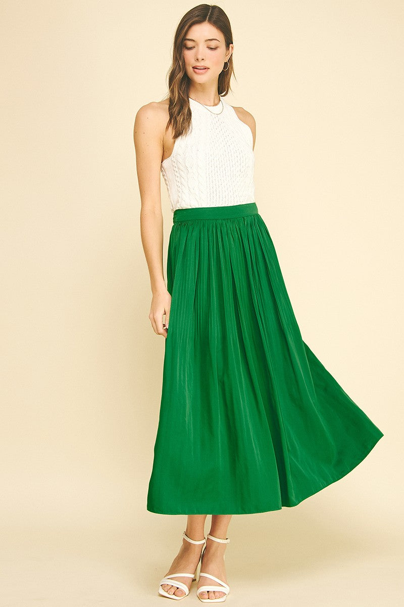 Woman wearing a green Maggy Pleated A-line Midi Skirt with a white sleeveless top and white heels.