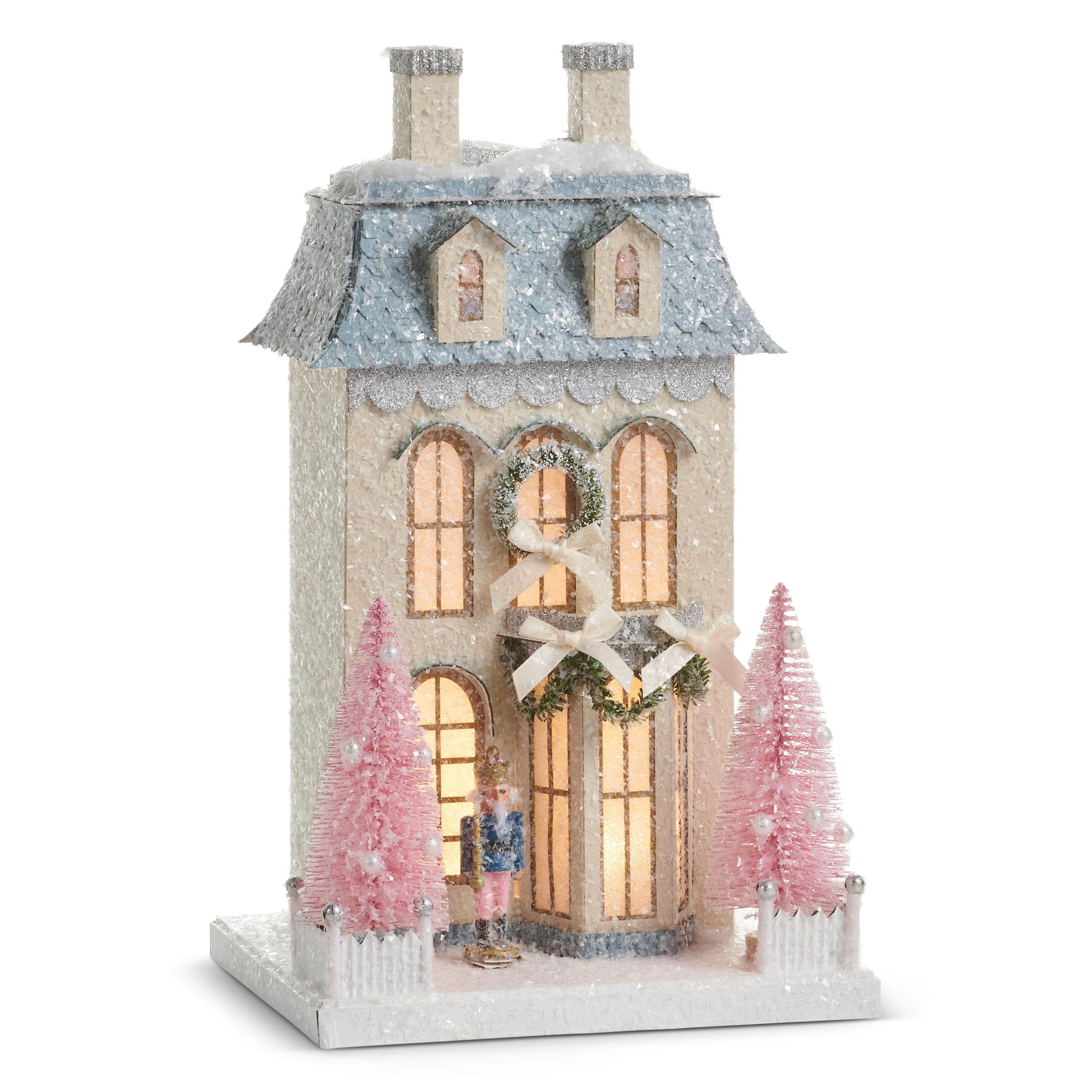 15-inch lighted paper nutcracker house with pink bottle brush trees and glittery snow accents.