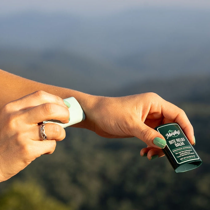 A person applies Murphy's Naturals Bite Relief Soothing Balm Stick to their arm outdoors.