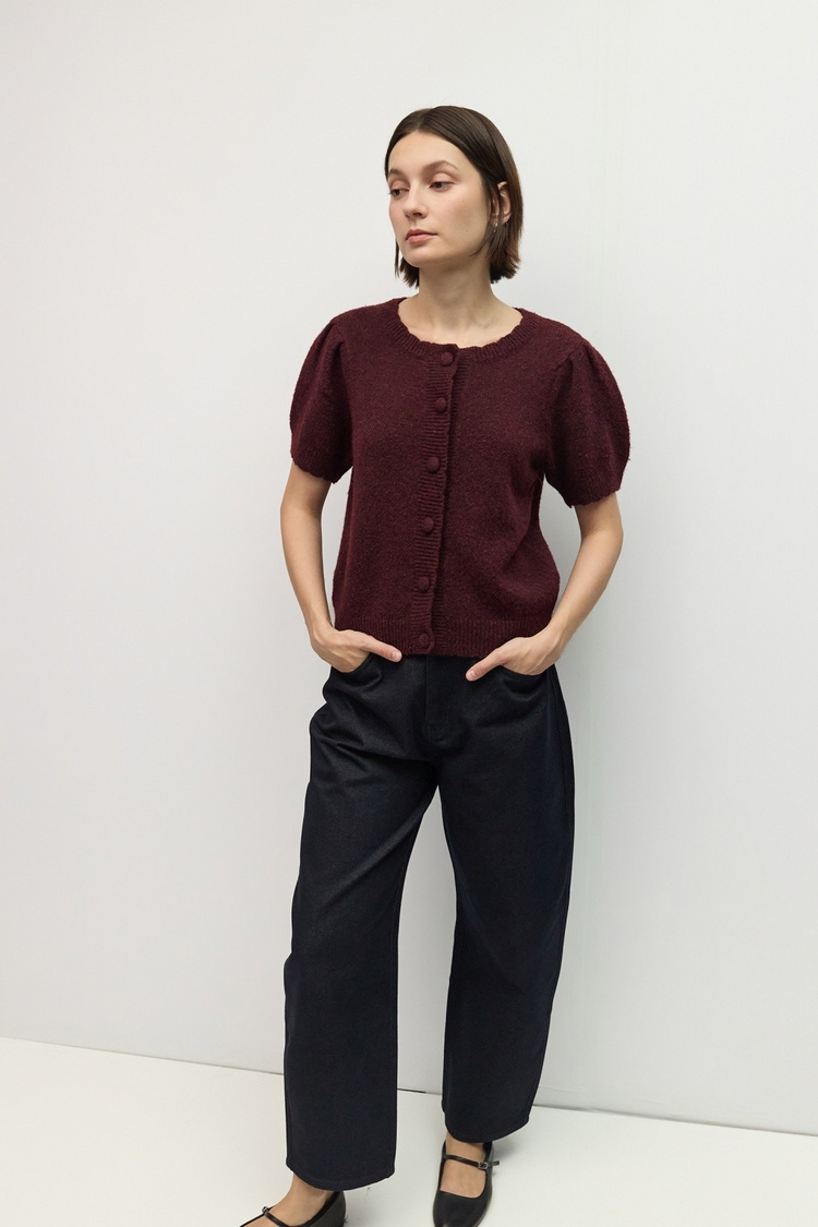 Woman wearing The Mary Kate Top, a burgundy short puff sleeve knit cardigan with black trousers.