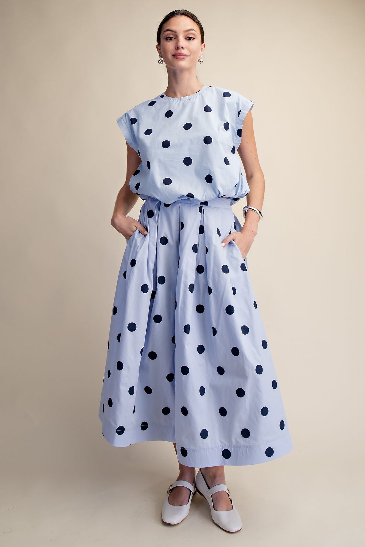 Woman wearing a light blue Cindy round neck bubble crop top with navy polka dots and matching skirt.