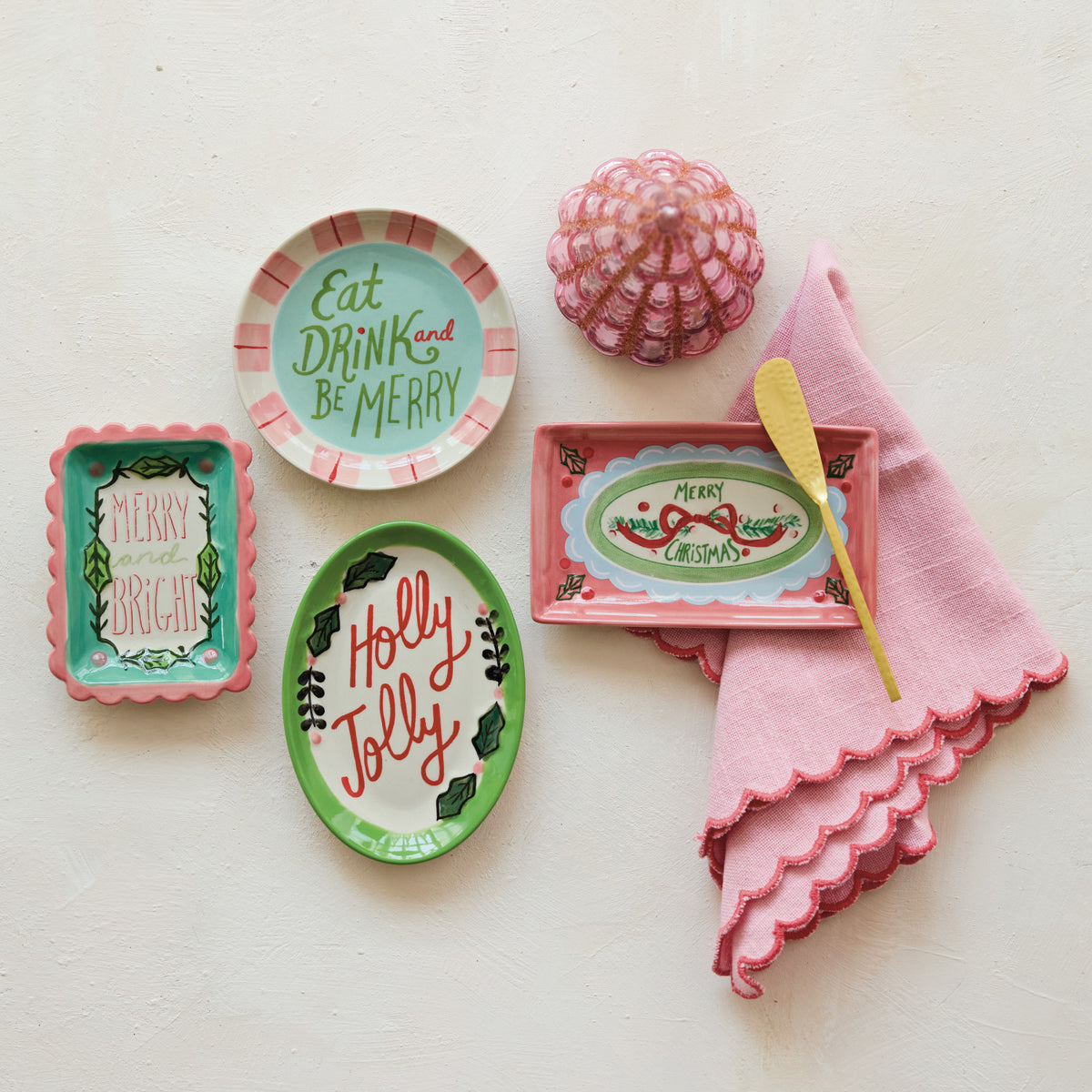 Assorted stoneware holiday dishes with festive sayings like 'Holly Jolly' and 'Merry Christmas'.
