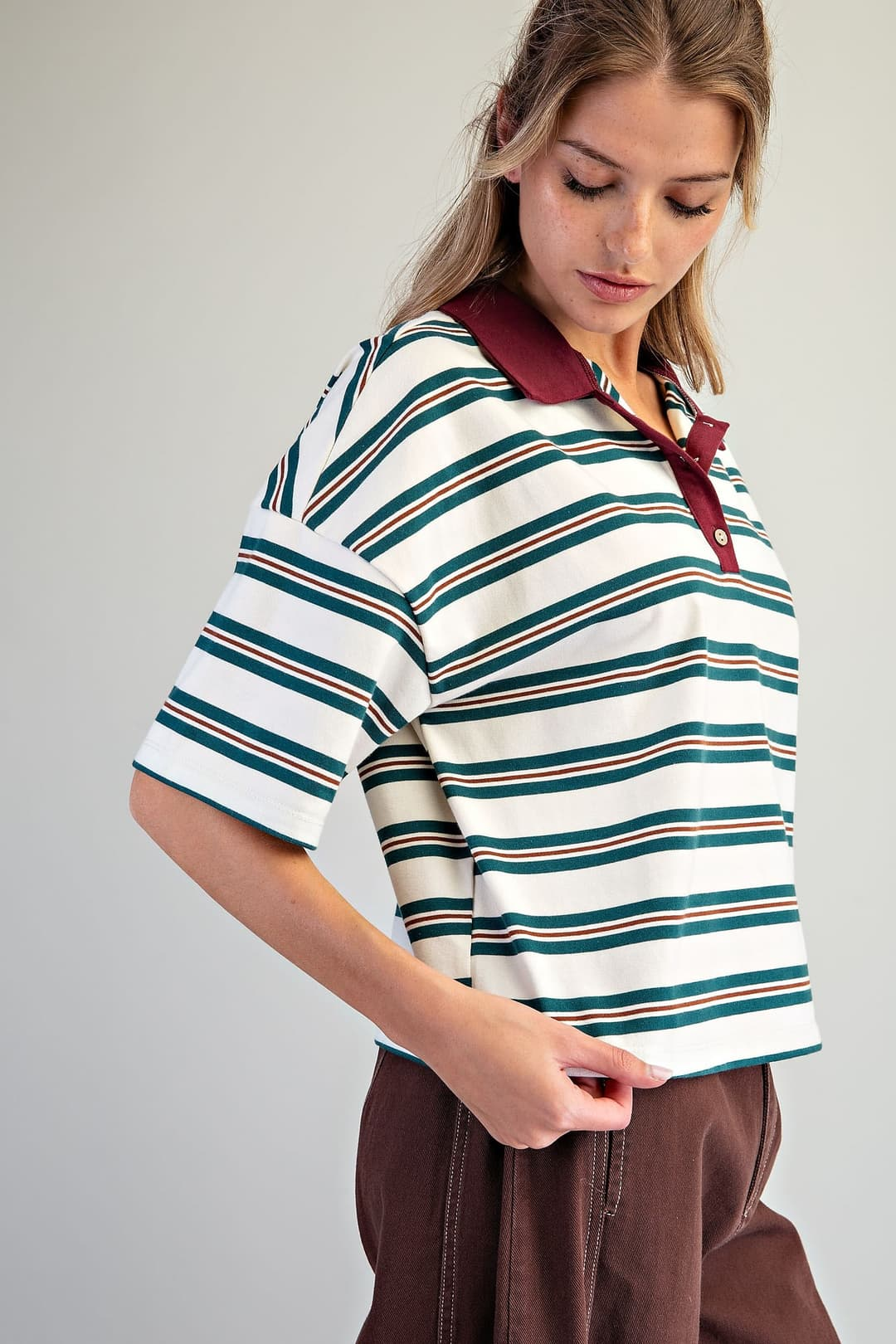 Woman wearing a boxy, oversized forest green and white striped polo top with a burgundy collar.