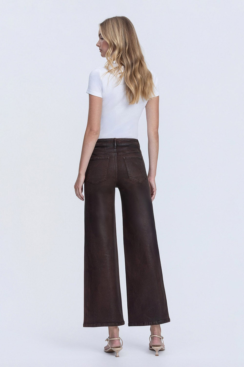Rear view of a model wearing dark brown Kitty high rise coated wide leg jeans and a white t-shirt.