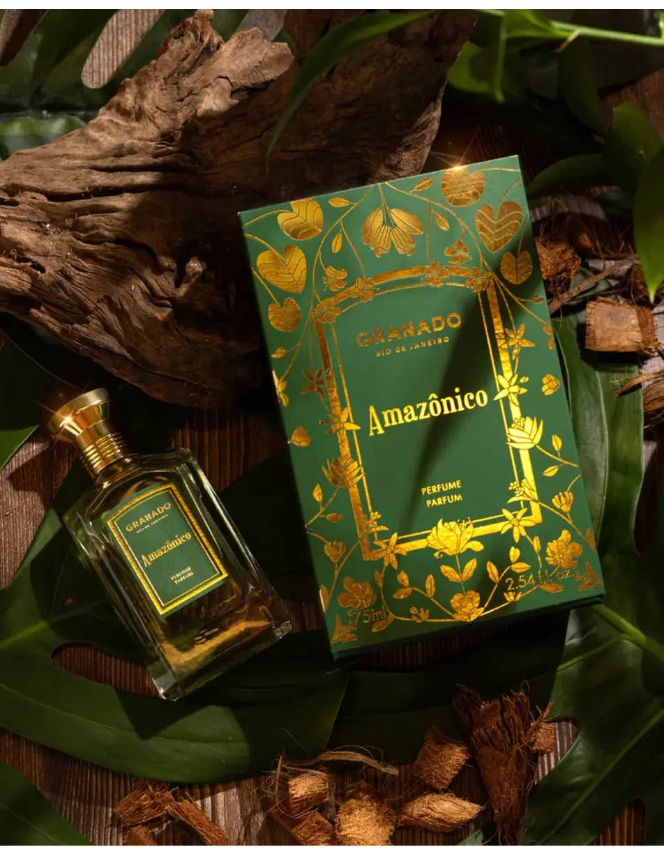 Amazônico Eau de Parfum bottle and green floral box on a rustic wood and leaf background.