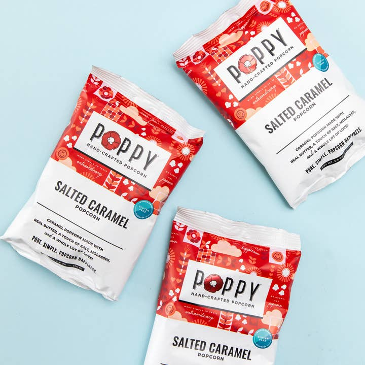 Three bags of Poppy Hand-Crafted Salted Caramel Popcorn on a light blue background.