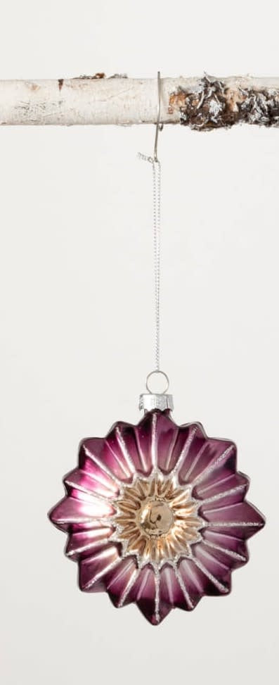 Purple and gold star-shaped glass witch eye ornament hanging from a birch branch.