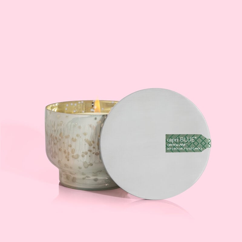 Crystal Pine Holiday Mercury Inverted Jar candle with silver lid and lit flame on pink background.
