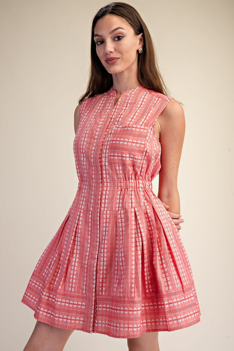 Woman wearing a sleeveless coral pink Clara Boho Shirt Dress with white floral embroidery.