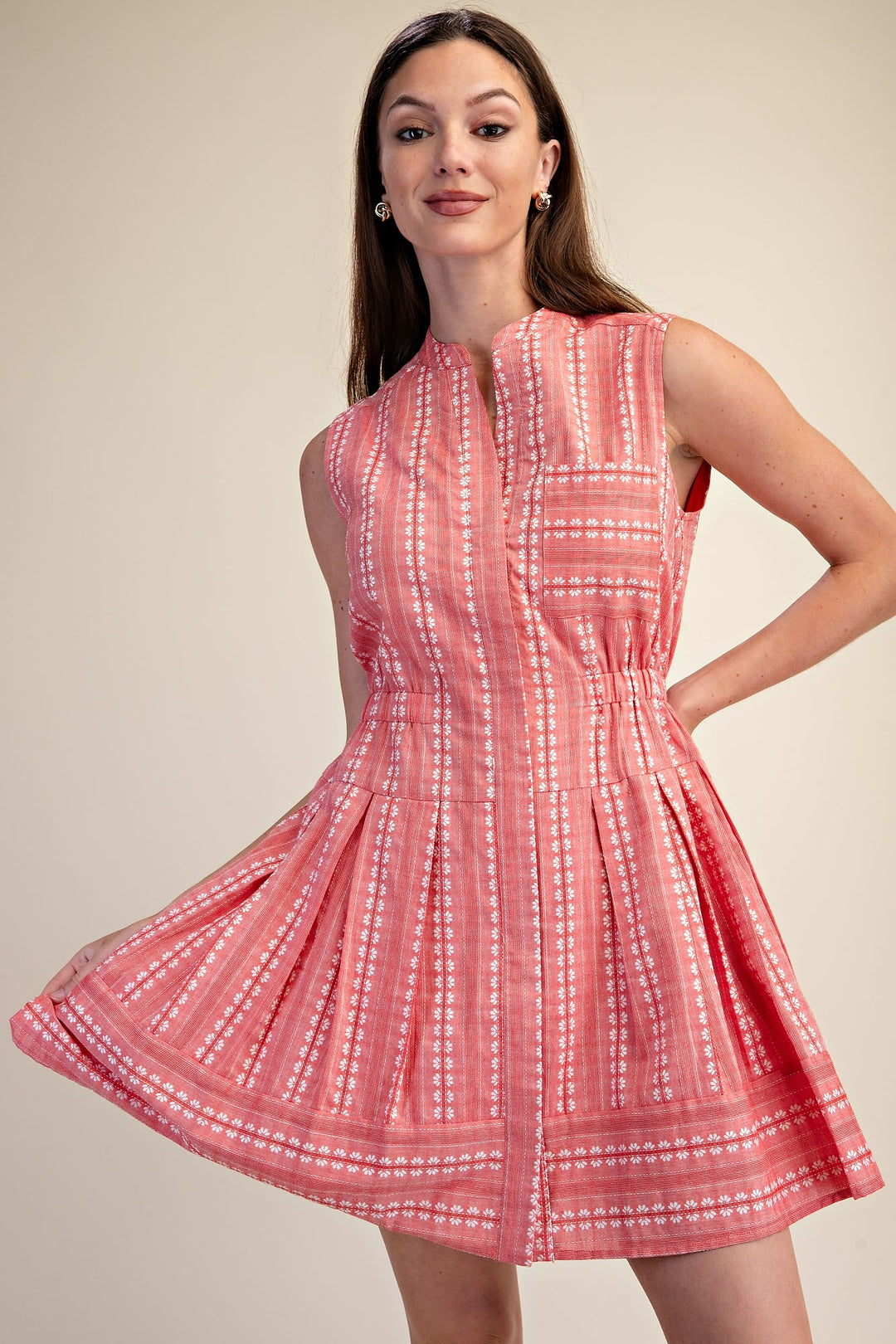 Woman wearing a sleeveless coral pink boho shirt dress with white embroidery and a pleated skirt.