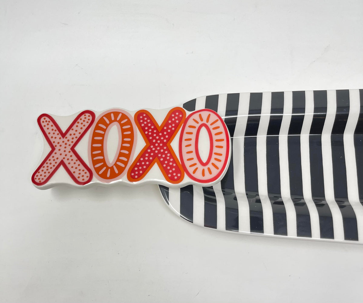 White ceramic attachment with red and orange 'XOXO' text, placed on a black and white striped tray.