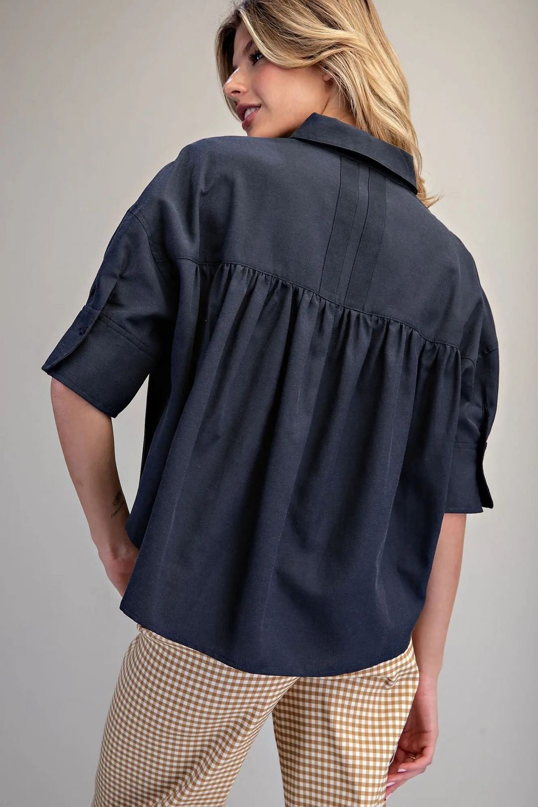 Back view of a woman wearing a navy blue Lou Button Down Short Sleeve Shirt with pleated back detail.