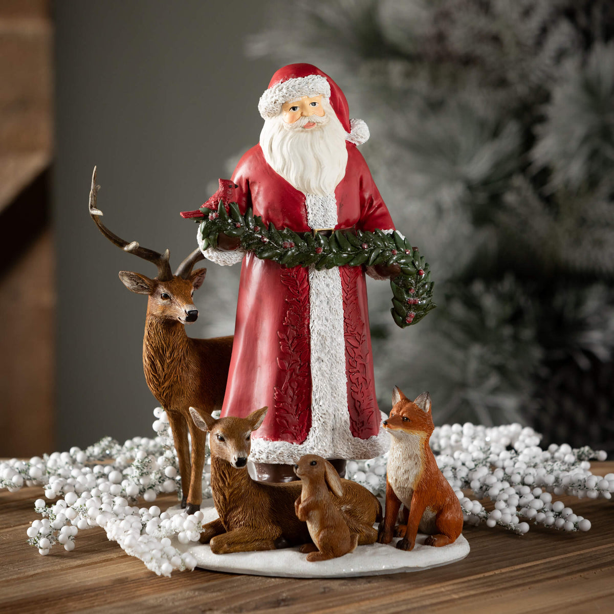 Santa figurine in a red coat holding a garland, surrounded by a deer, fawn, rabbit, and fox.