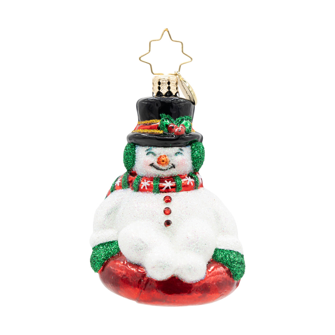 Snowman Christmas ornament wearing a black top hat and green earmuffs, sitting on a red snow tube.