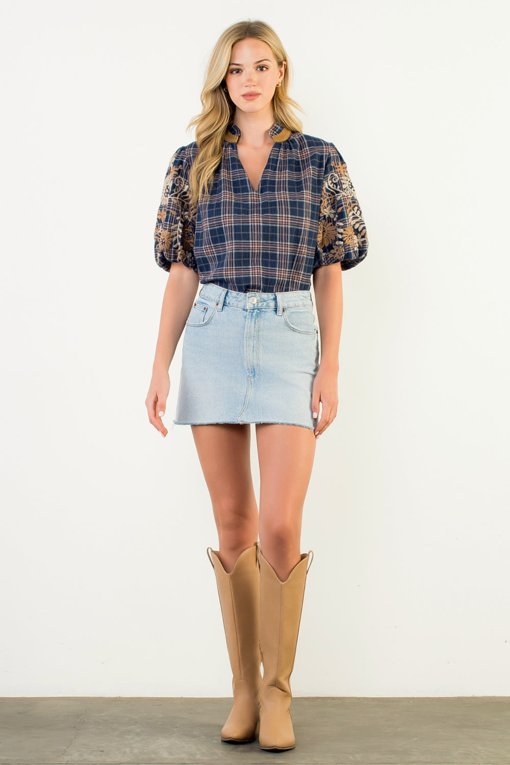 Woman wearing a Gwen blue gingham top with embroidered puff sleeves and a denim skirt.