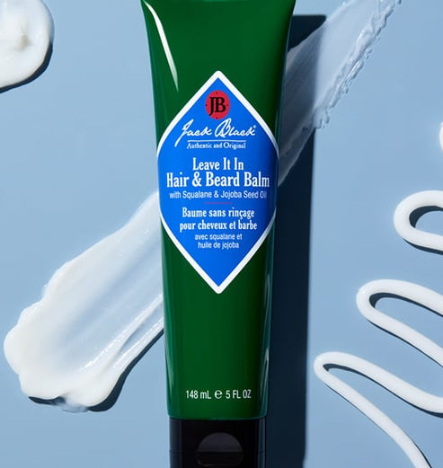 Jack Black Leave It In Hair & Beard Balm in a 5oz green tube surrounded by white cream swatches.