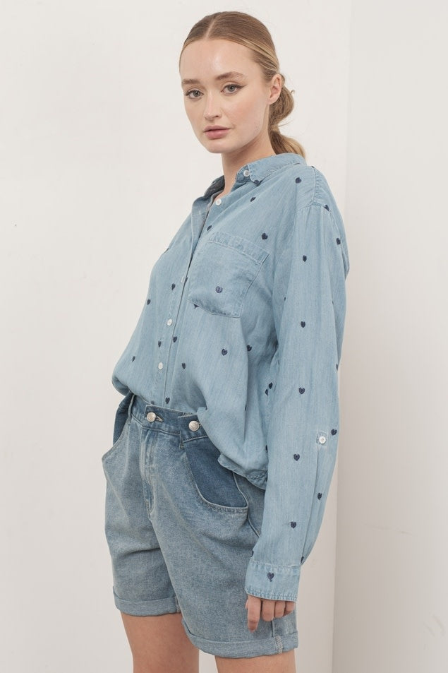 Side view of a denim oversized chambray shirt with heart embroidery detail on the chest.