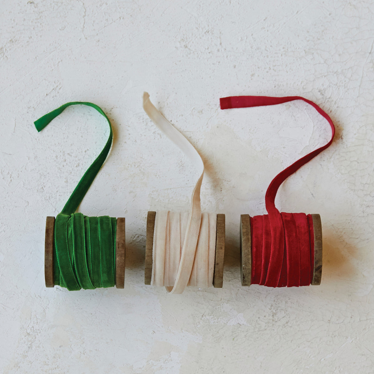 Three 10-yard velvet ribbons in green, cream, and red on individual wooden spools.
