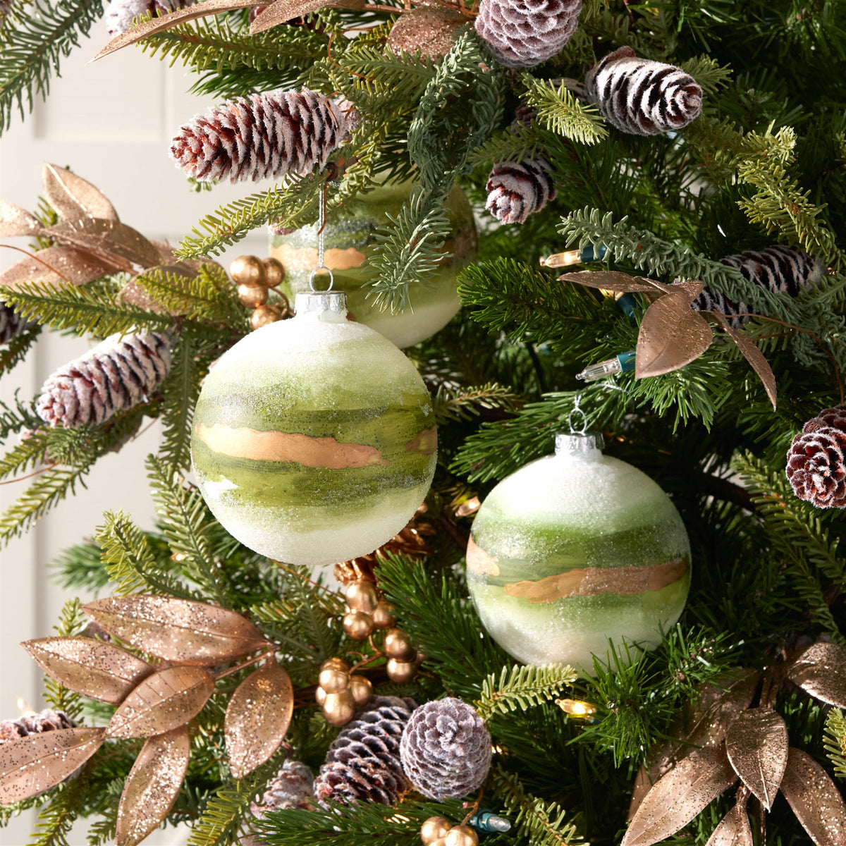 Three 4-inch glass ball ornaments with green and gold stripes on a decorated Christmas tree.