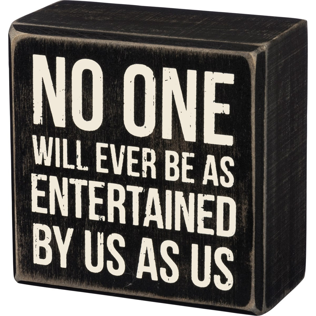 Black wooden box sign with white text reading 'NO ONE WILL EVER BE AS ENTERTAINED BY US AS US'.