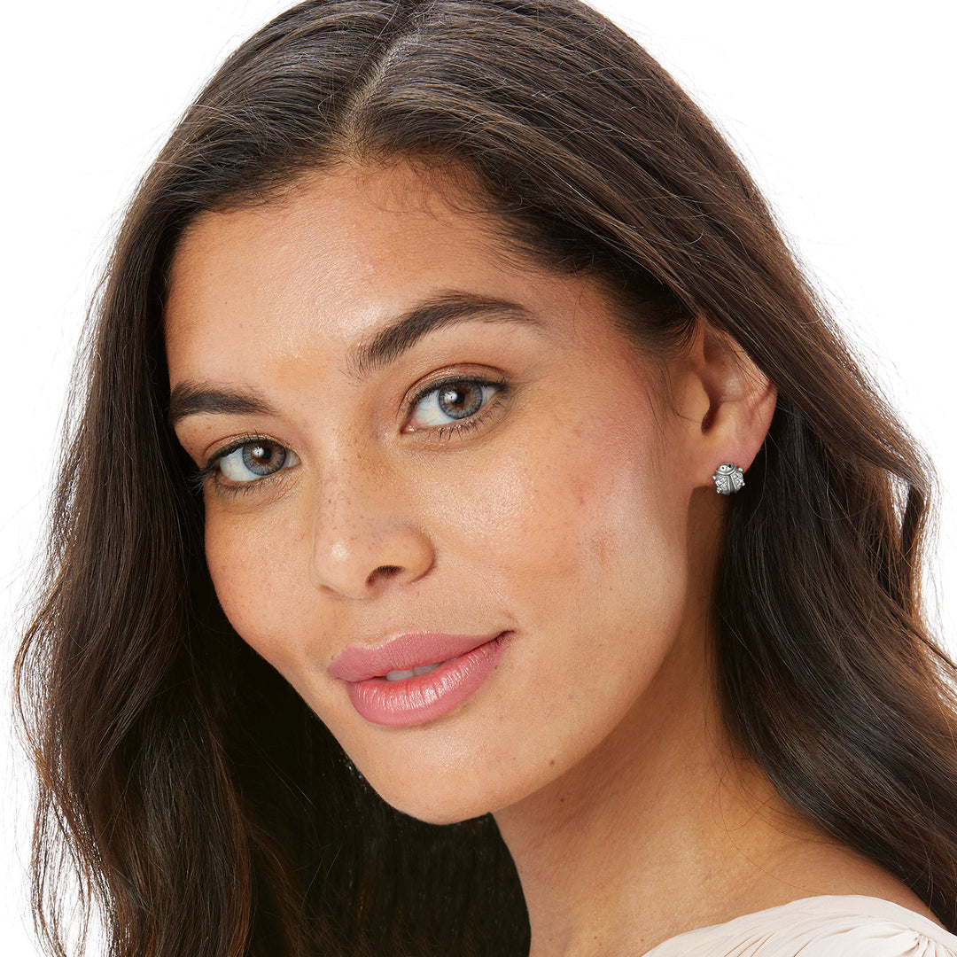 A woman wearing the Lady Luck Mini Post Earrings, which are silver-plated ladybug-shaped studs.