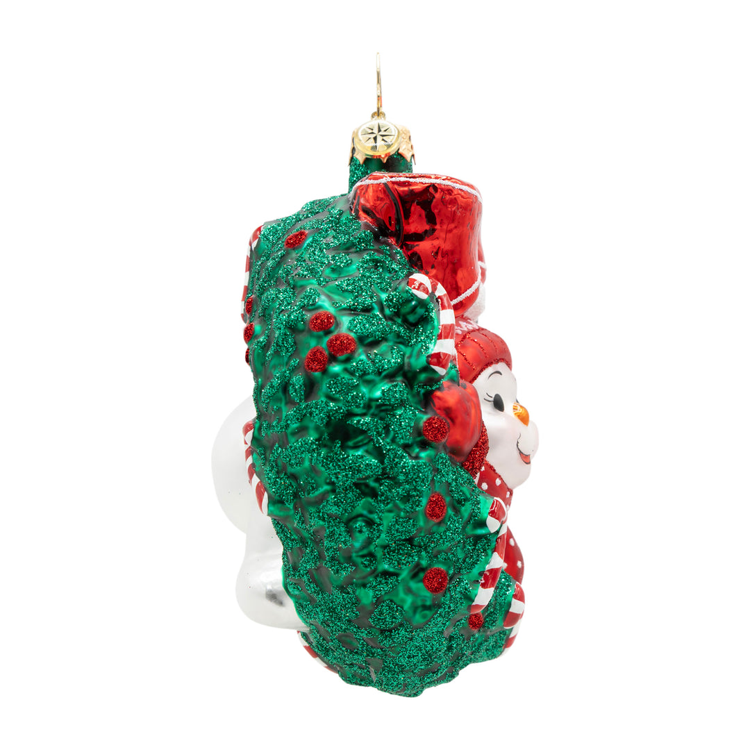 Side view of a snowman ornament inside a green glittery wreath with candy canes and red berries.