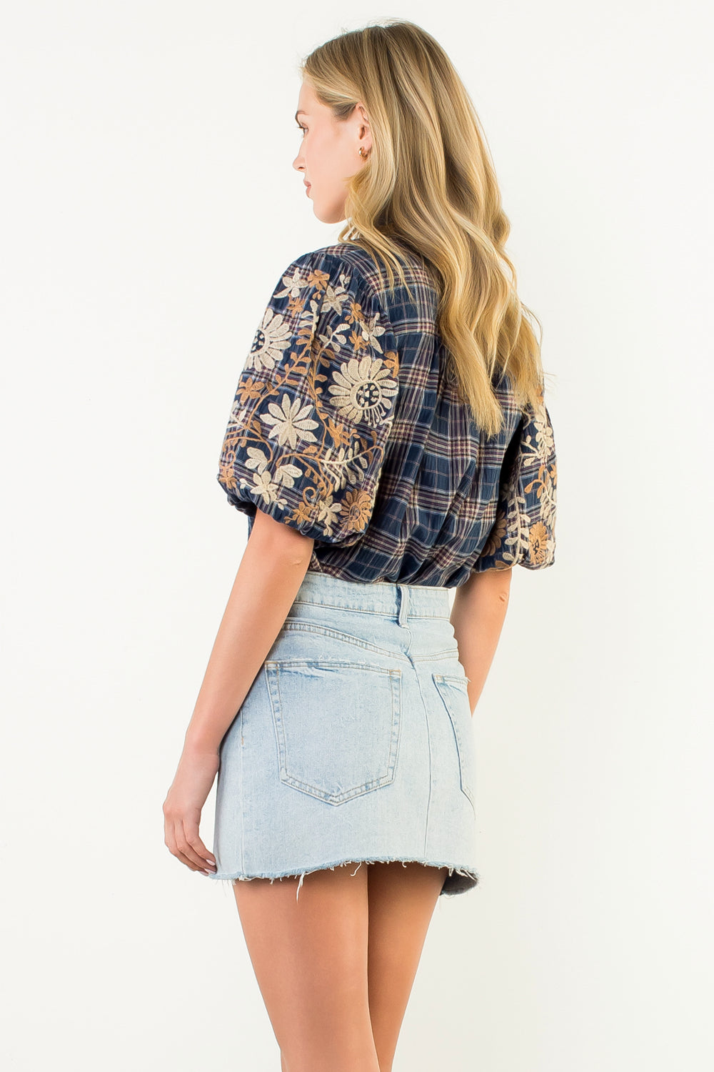 Back view of a woman wearing a Gwen navy gingham top with floral embroidered puff sleeves.