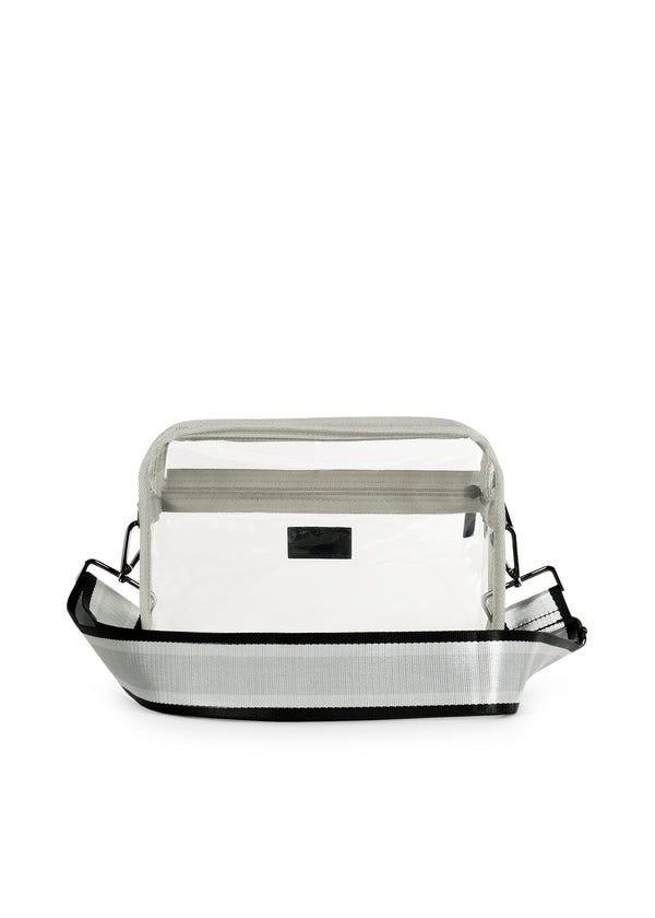 Drew Clear Crossbody bag with a transparent vinyl body and a striped grey and black shoulder strap.