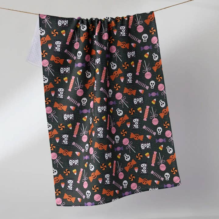 Halloween tea towel with a black background and a pattern of skulls, candy, and 'BOO!' text.