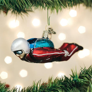 Glass skydiver ornament in a red jumpsuit and silver helmet hanging from a Christmas tree branch.