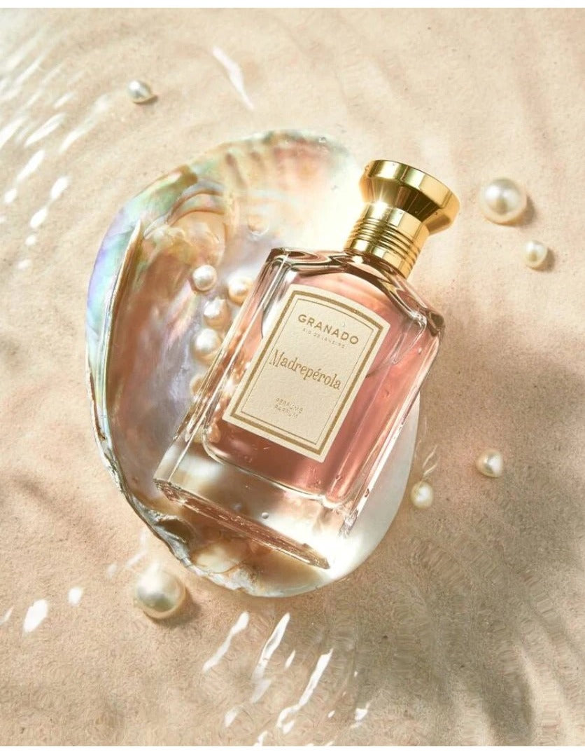 Madrepérola Eau de Parfum bottle resting in a large seashell on sand with scattered pearls.