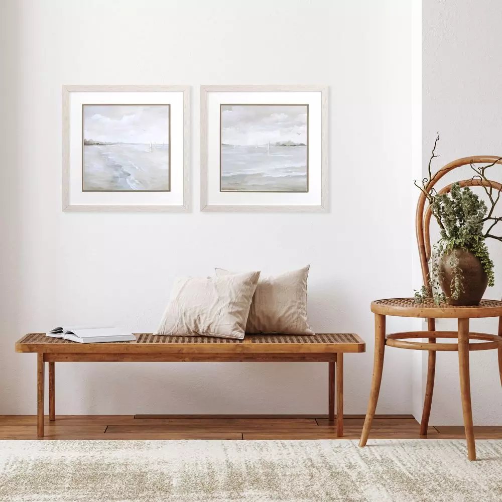 Two framed abstract paintings of sailboats on a calm sea, displayed above a wooden bench with two pillows.
