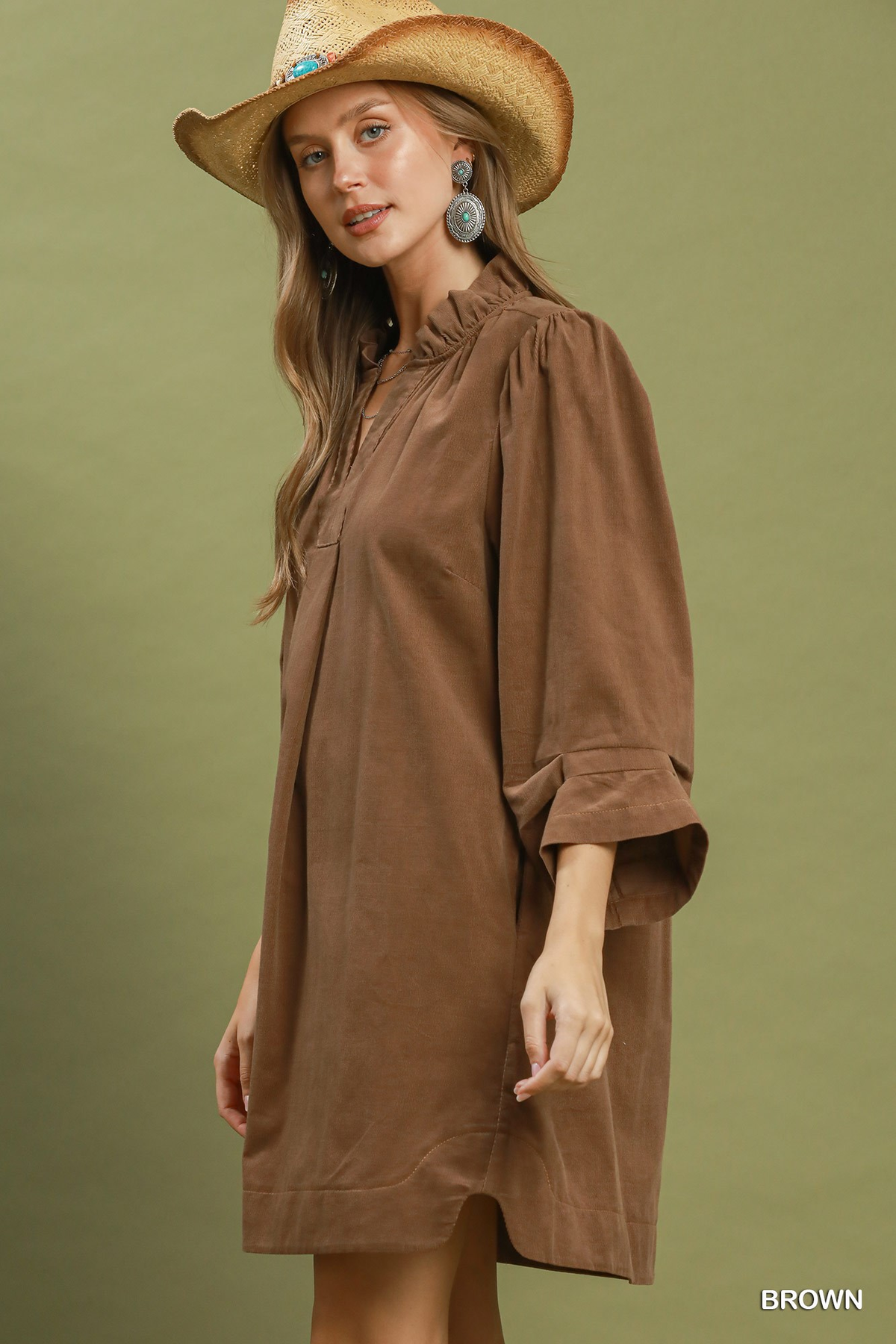 Woman wearing a brown corduroy split neck puff sleeve shift dress and a straw hat.