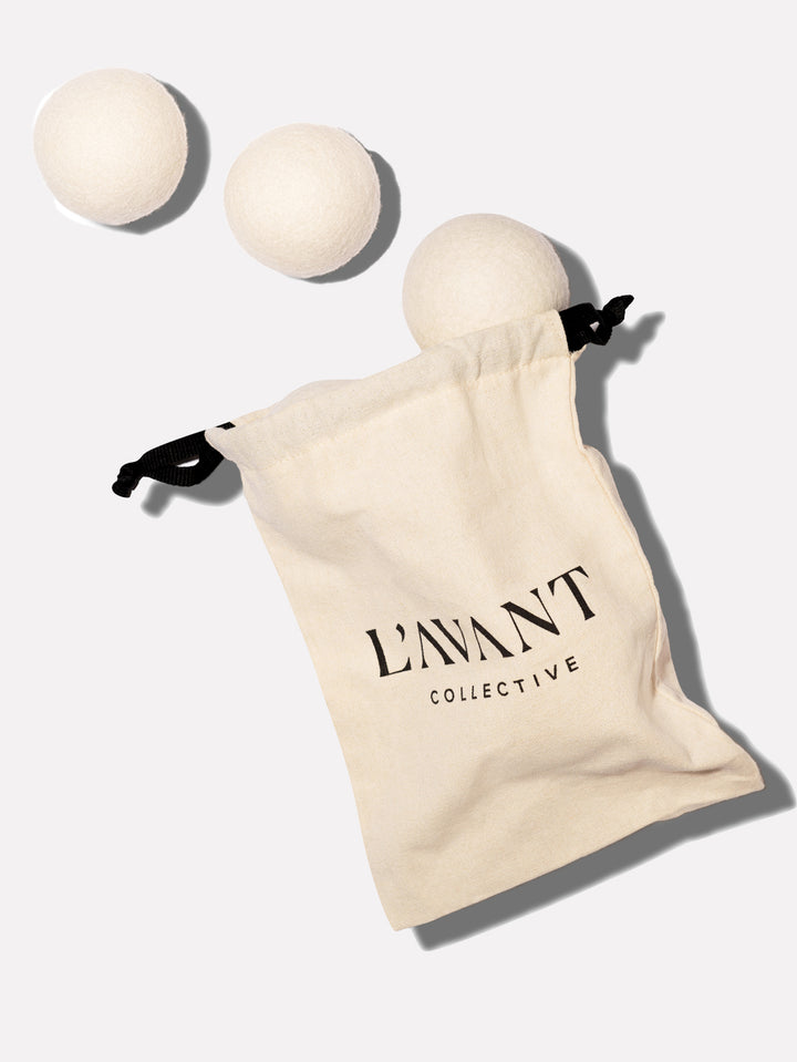 Three white wool dryer balls next to a cream-colored drawstring bag with the L'AVANT logo.